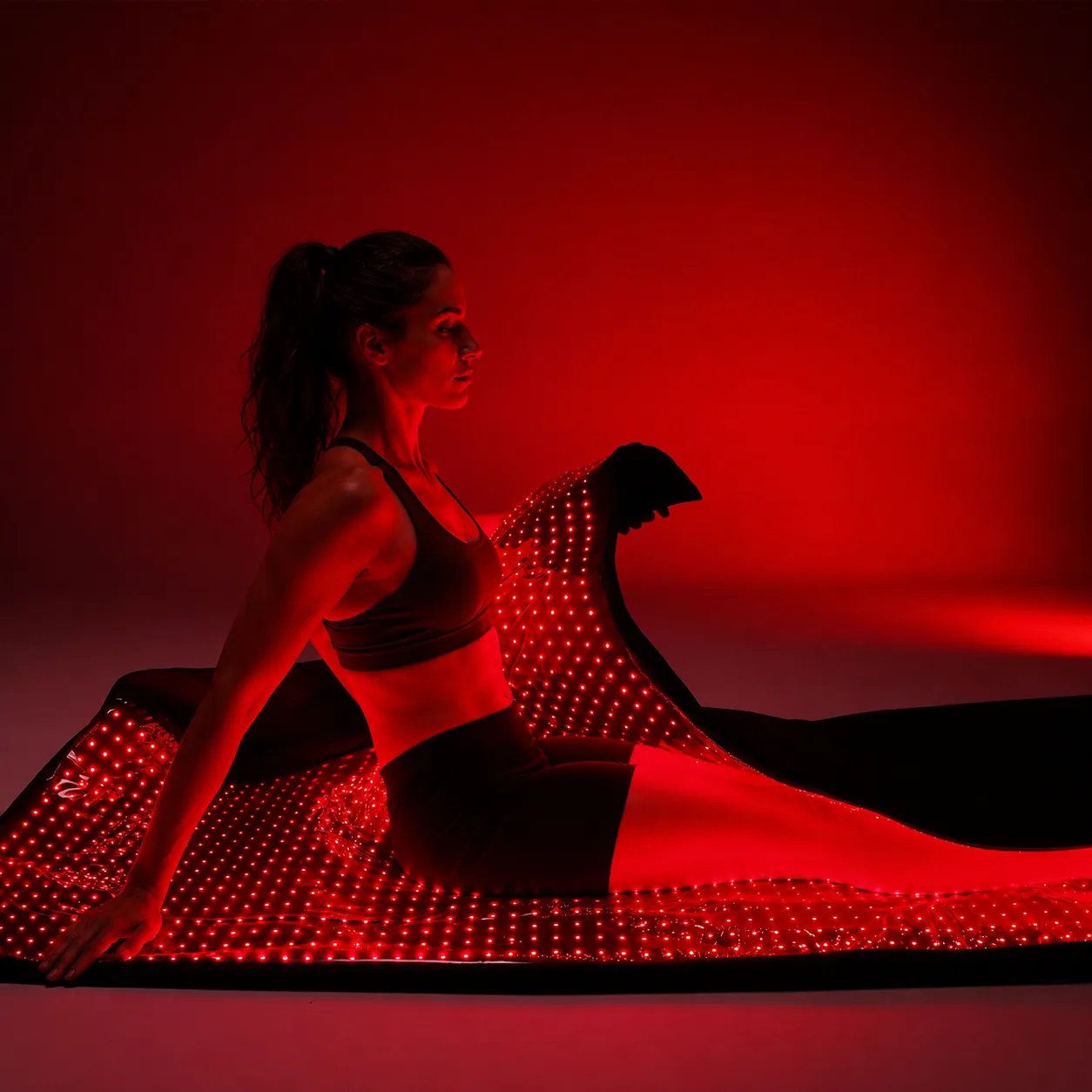 A woman seated on the red-light mat as it wraps up around her body