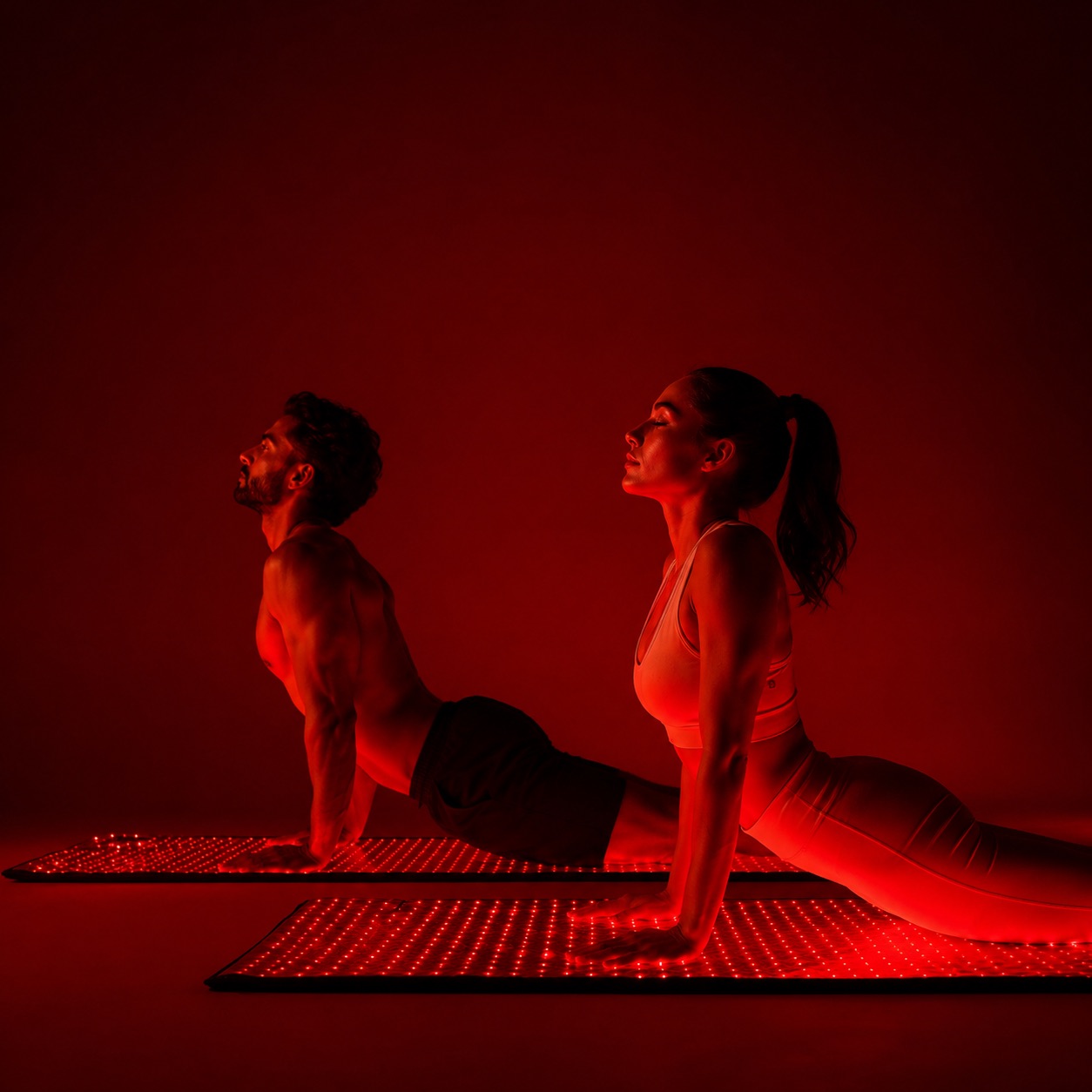 Two people in an upward stretch on separate lit Rubaris Recovery Mats.